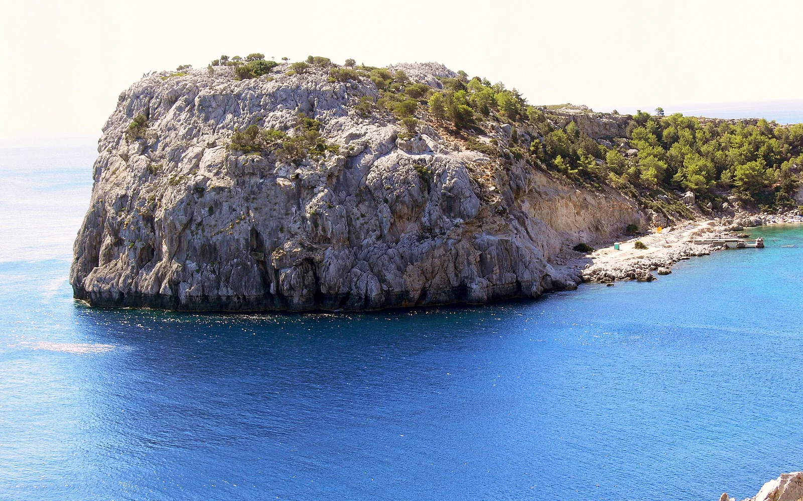 The clear water and rocky coast of Anthony Quinn Bay